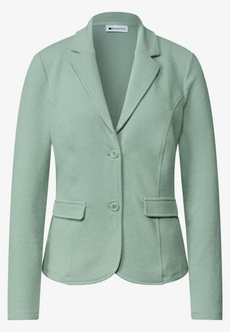 Grüner Damenblazer mit zwei Knöpfen, Reverskragen und aufgesetzten Taschen.