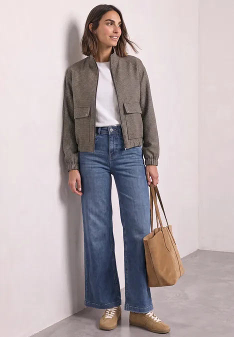 Frau in weit geschnittenen Jeans, weißem T-Shirt, kurzer grüner Jacke und brauner Tasche