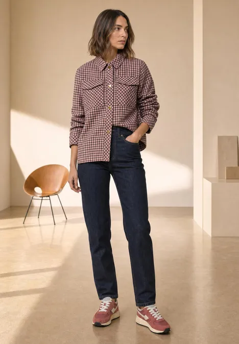 Frau in kariertem Mantel, dunkle Jeans und rote Sneaker in minimalistischem Raum.