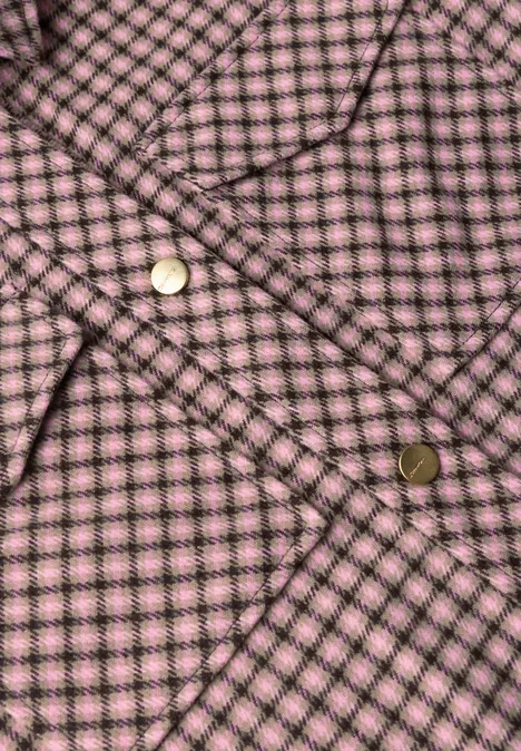 Nahaufnahme eines rosa-karierten Stoffes mit goldfarbenen Druckknöpfen.