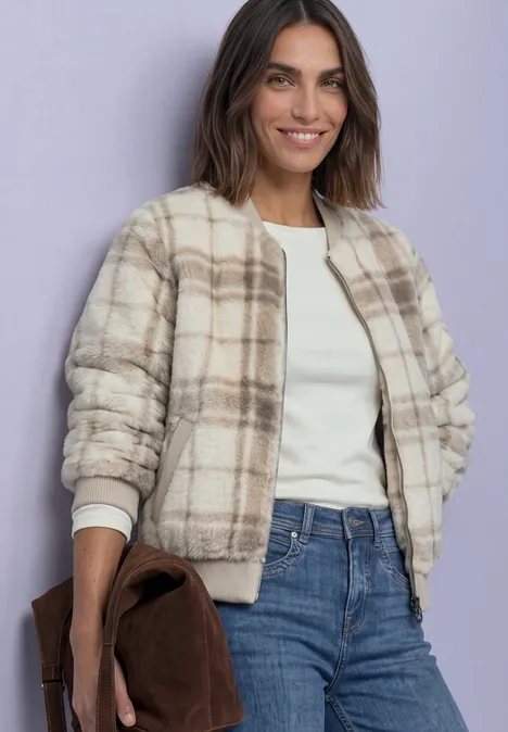 Frau trägt karierte Teddyjacke, weiße Bluse, Jeans und hält braune Tasche.
