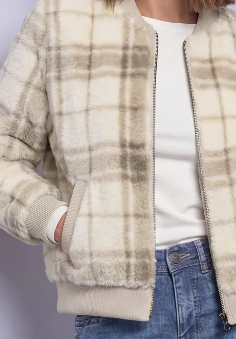 Frau in cremefarbener, karierten Kuscheljacke, weißem T-Shirt und blauen Jeans.