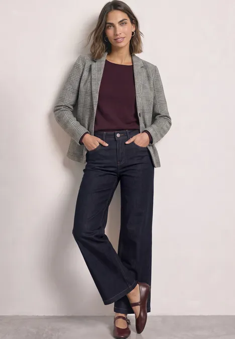 Blazer mit Karomuster und Knöpfen Black Frau steht in grauem Blazer, dunkelrotem Top, weiten Jeans und braunen Slippern.