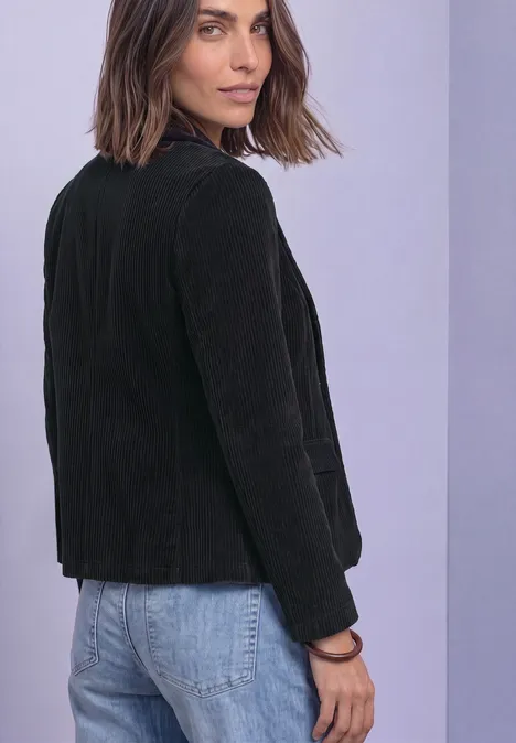 Femme en veste noire en velours côtelé et jean bleu regarde par-dessus son épaule.