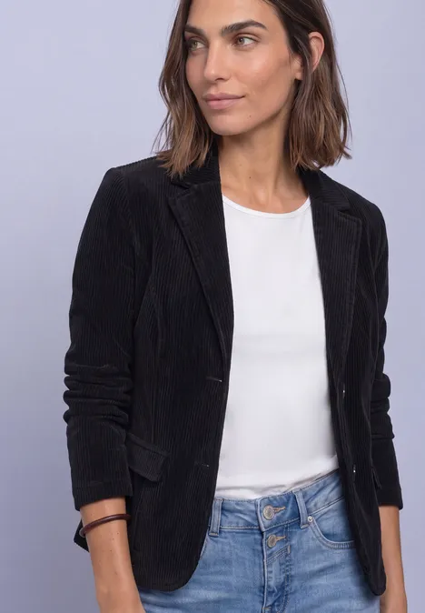 Femme en blazer noir, haut blanc et jean devant un fond neutre.