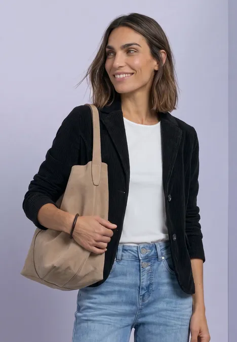 Femme souriante en blazer noir, t-shirt blanc, jean bleu et sac beige.
