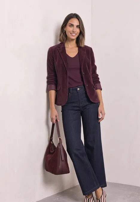 Femme en blazer velours bordeaux, top assorti, jeans évasés foncés et sac coordonné.