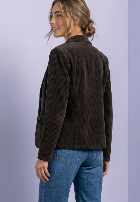 Une femme en jean et veste en velours côtelé marron sourit en regardant par-dessus son épaule.