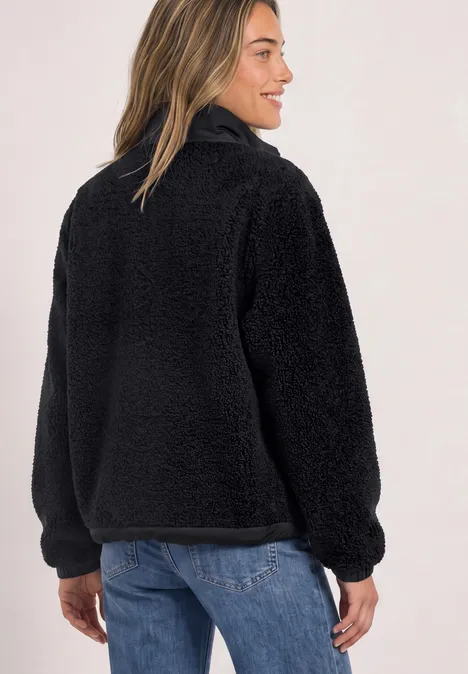 Femme portant une veste en polaire noire, style teddy, col montant et demi-fermeture éclair arrière.
