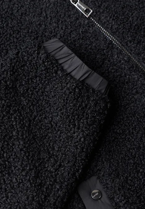 Gros plan sur un vêtement noir en molleton effet peluche avec fermeture éclair, fronces et bouton.