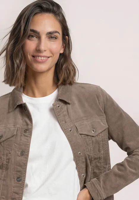 Een glimlachende vrouw met halflang bruin haar draagt een wit shirt en een bruine jas voor een lichte achtergrond.