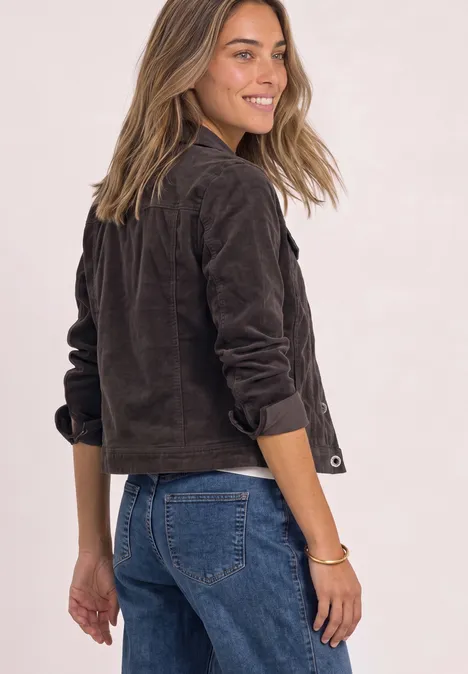 Vrouw kijkt lachend over haar schouder, draagt korte bruine jas en blauwe jeans