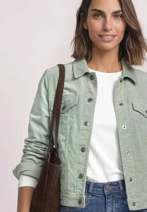 Jonge vrouw in een groen spijkerjack, wit T-shirt en jeans, met een bruine schoudertas.