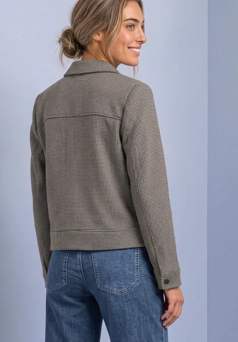 Achteraanzicht van een vrouw in een grijs jasje en blauwe spijkerbroek, glimlachend en naar rechts kijkend.