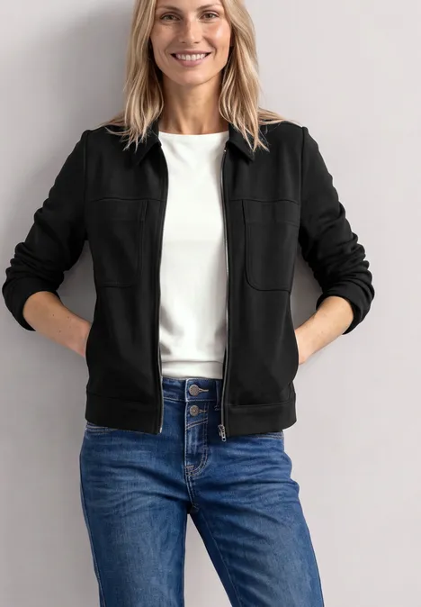 Jas met overhemdkraag en borstzakken Black Vrouw in zwart jack en spijkerbroek, lachend voor een neutrale achtergrond.