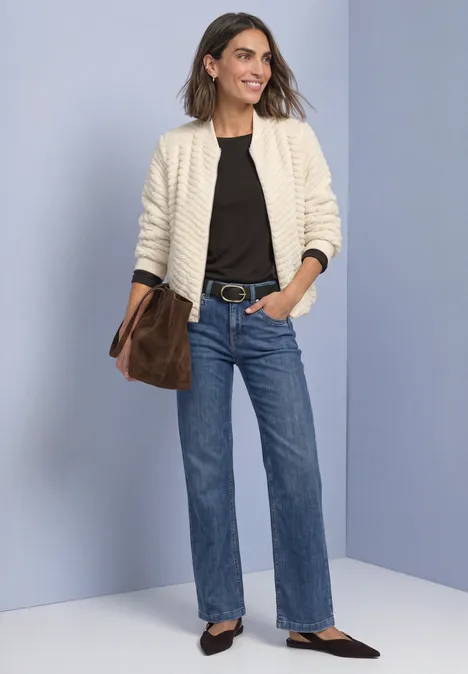 Teddy-Jacke mit Zick-Zack-Struktur pure beige Frau in weißer Jacke, schwarzem Oberteil, blauen Jeans und schwarzen Schuhen, trägt eine braune Tasche.