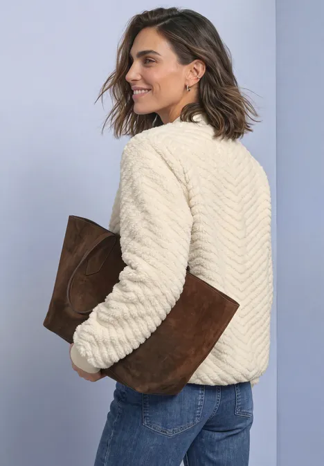 Teddy-Jacke mit Zick-Zack-Struktur pure beige Frau im cremefarbenen, strukturierten Teddy-Pullover hält eine braune Wildleder-Clutch.