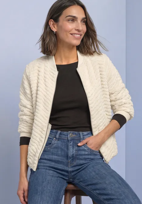 Teddy-Jacke mit Zick-Zack-Struktur pure beige Frau in weißer gesteppter Jacke, schwarzem Top und Jeans, lächelt vor hellem Hintergrund.