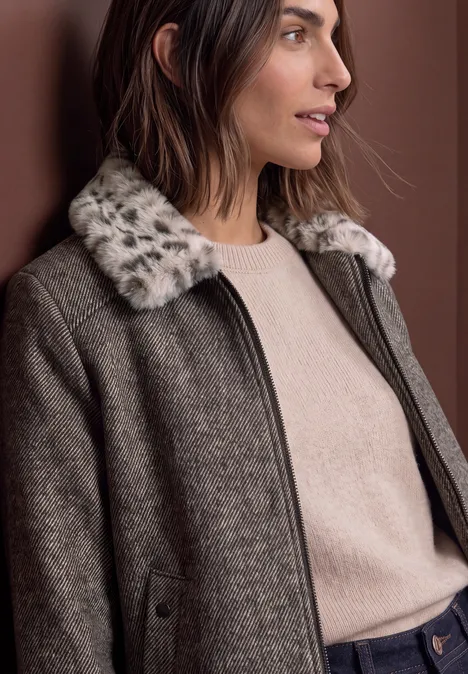 Vrouw draagt een bruin wollen mantel met een bontkraag en een lichtbeige trui.