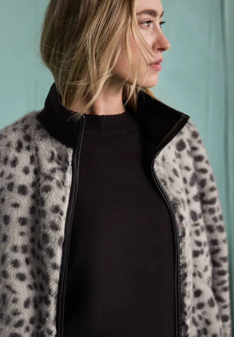 Fake Fur Jacke mit Animal Print black coffee Blonde Frau im Profil mit grauem, gepunktetem Mantel und schwarzem Oberteil vor neutralem Hintergrund.