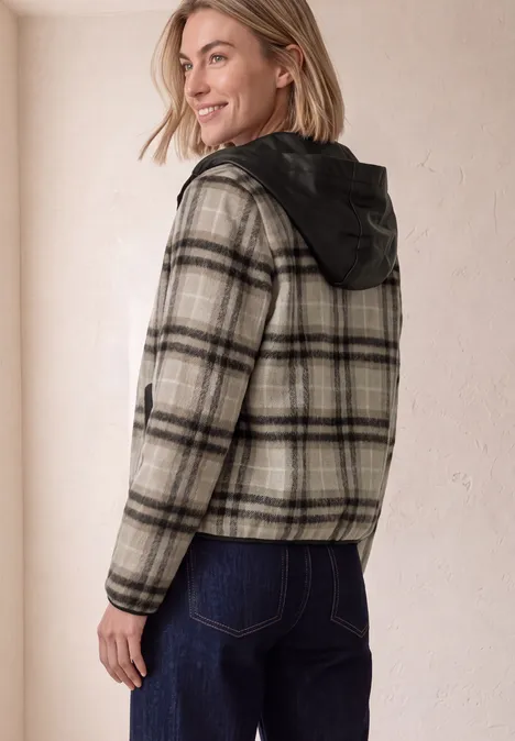 Jacke mit Wollanteil und Kapuze black coffee Frau in karierter Jacke mit Kapuze und Jeans, lächelnd über die Schulter blickend vor heller Wand.