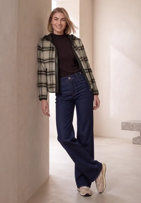 Jacke mit Wollanteil und Kapuze black coffee Modell in minimalistischer Umgebung lehnt lässig: karierte Jacke, schwarzer Pullover, weite blaue Jeans, weiße Sneaker.