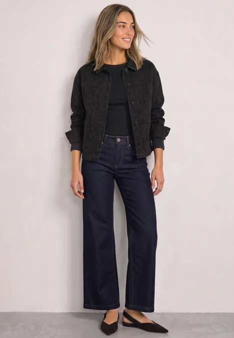 Jeansjacke mit Leo-Muster und Kragen Leo Print Washed Frau mit blonden Haaren trägt schwarze Jacke, Shirt und weite Jeans vor hellem Hintergrund.