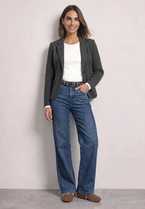 Een vrouw draagt een spijkerbroek, een grijze blazer, een wit shirt en bruine schoenen.