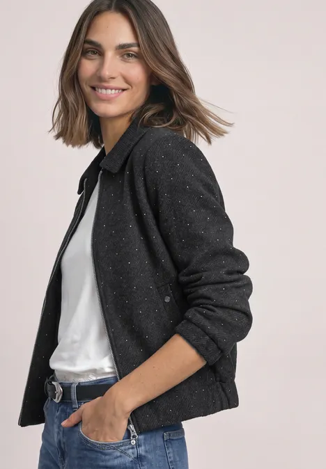 Une femme souriante aux cheveux bruns porte un gilet noir et un t-shirt blanc.