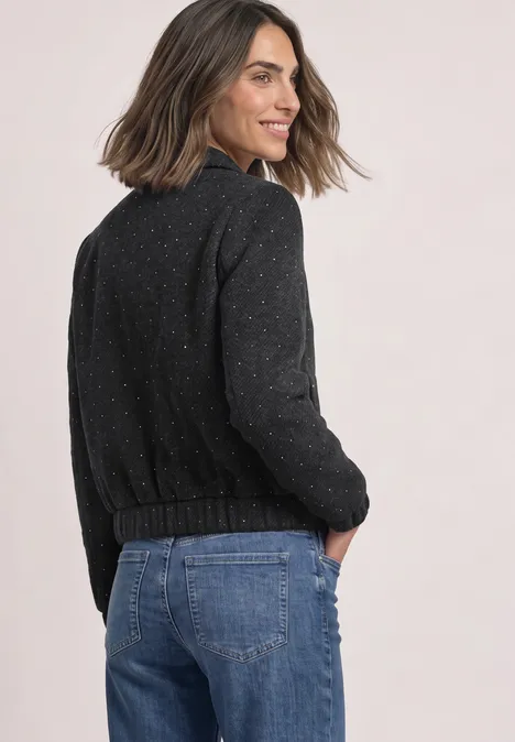 Femme souriante en pull sombre et jean regardant par-dessus l’épaule.