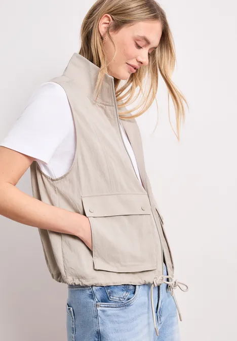 Vrouw met wit T-shirt en beige mouwloos vest met zakken en tunnelkoord