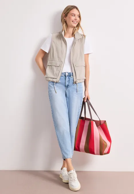 Vrouw met vest, t-shirt, jeans en grote rode tas.