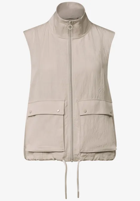 Beige mouwloze bodywarmer met opstaande kraag, ritssluiting, klepzakken en verstelbare zoom.