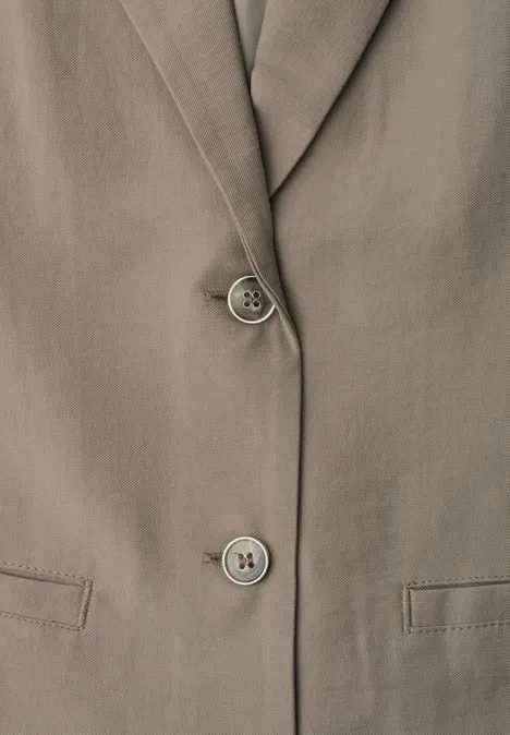 Nahaufnahme einer taupefarbenen Blazer-Jacke mit Reverskragen, zwei Knöpfen und Pattentaschen.
