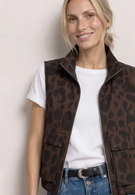 Femme blonde souriante en t-shirt blanc et gilet léopard marron, ceinture noire.