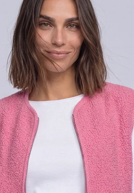 Eine lächelnde Frau mit dunklen Haaren trägt eine rosa Strickjacke und ein weißes T-Shirt.