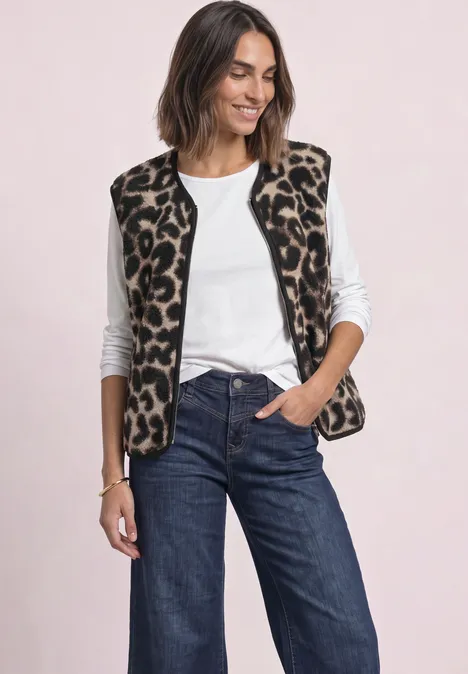 Frau in weißem Top und Jeans trägt ärmellose Weste mit Leopardenmuster und lächelt