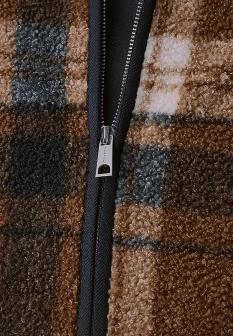 Nahaufnahme eines Reißverschlusses an kariertem braunem Fleece mit schwarzem Reißverschlussband