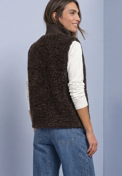 Frau von hinten in brauner Fleece-Weste, weißem Langarmshirt und blauer Jeans