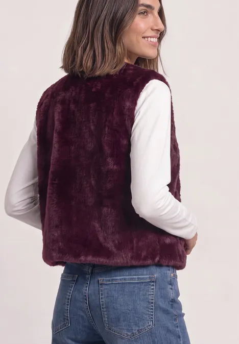 Frau von hinten in dunkelvioletter Kunstfellweste, weißem Oberteil und Jeans.