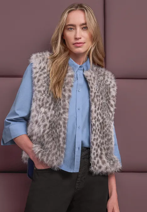 Fake-Fur Weste mit Zipper und Taschen clay sand Frau trägt blaue Bluse und graue Kunstfellweste, steht mit Händen in den Taschen vor gepolsterter Wand.