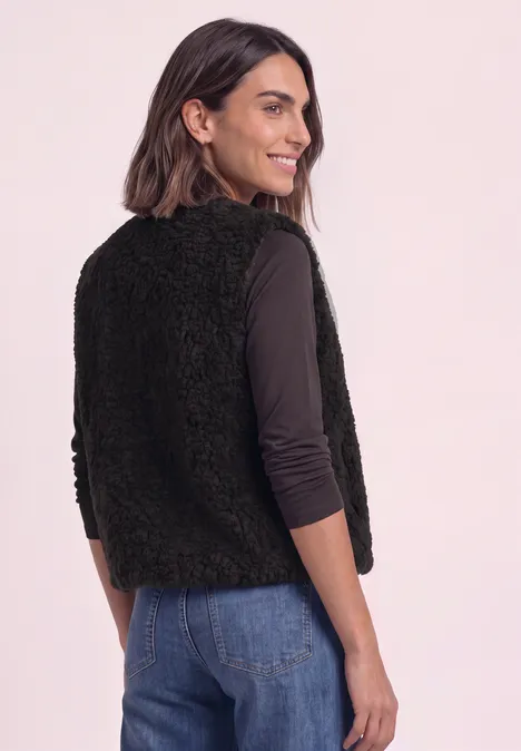 Frau im Profil trägt schwarze, flauschige Weste über langärmligem Top und Jeans.
