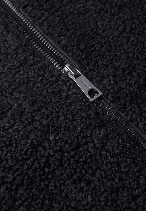 Nahaufnahme eines schwarzen Teddy-Fleece-Stoffs mit silbernem Metallreißverschluss.