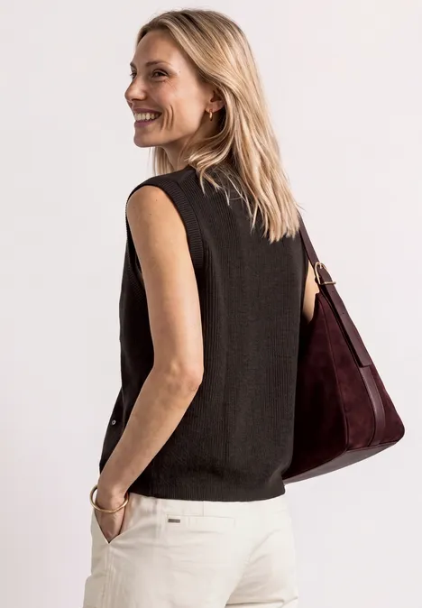 Vrouw in zwart mouwloos topje en witte broek, lachend omkijkend met een donkerrode tas over haar schouder.