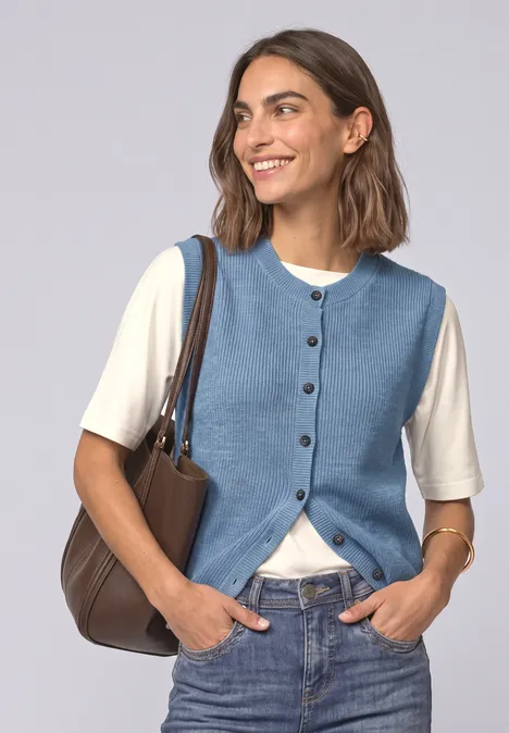 Strickweste mit Rundhals und Knopfleiste northern blue mel. Frau mit blauer Weste, weißem Shirt, Jeans und brauner Tasche lächelnd in die Kamera.