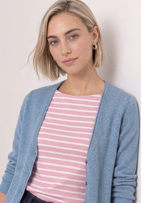 Cardigan à col en V et patte de boutonnage northern blue mel. Jeune femme aux cheveux blonds courts porte un t-shirt rayé rose et blanc et un cardigan bleu clair.