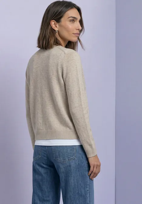 Cadigan met V-hals en knoopsluiting clay sand mel. Rückansicht einer Frau mit beigem Pullover, weißem Shirt und blauer Jeans vor lila Hintergrund.
