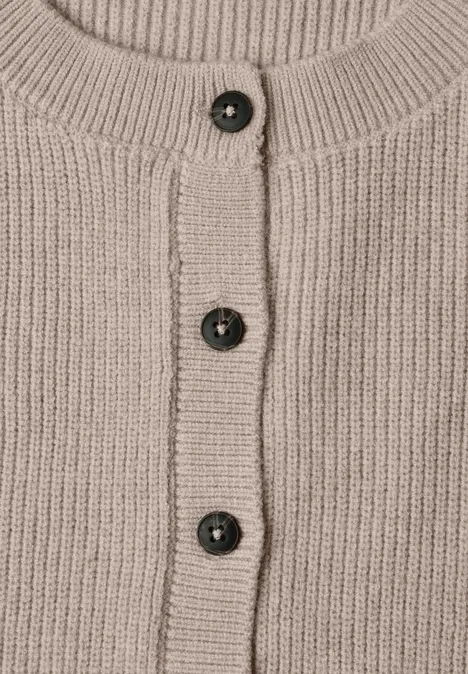 Beige gebreid vest met geribde boord en drie donkere knopen in het midden.