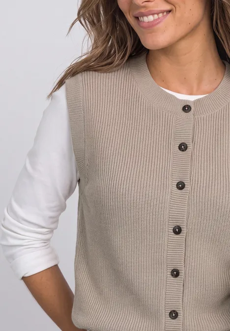 Vrouw glimlacht in beige geribbeld knoopvest over wit shirt met lange mouwen