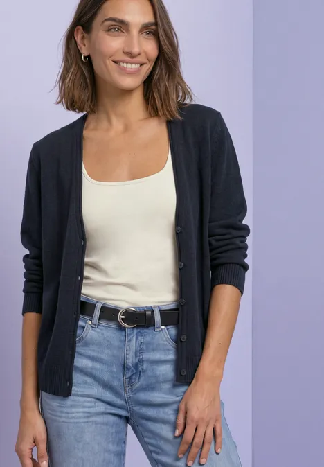 Cardigan à col en V et patte de boutonnage darkest blue Femme en gilet noir, débardeur beige et jean devant un fond violet.